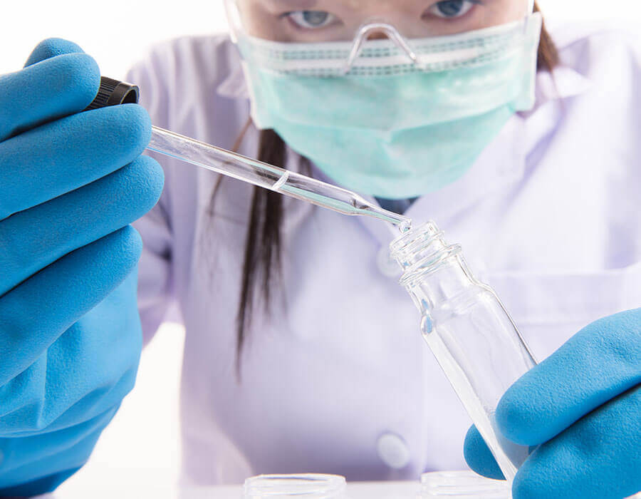 Closeup of a doctor in lab coat and mask inspecting a healthcare tube.